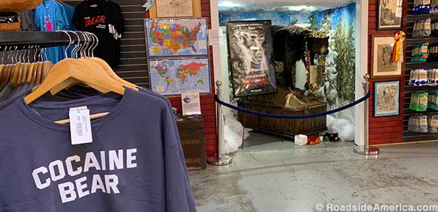 Cocaine Bear swag, visitor maps, and shrine. Offerings are left on the floor beneath the bear's feet.